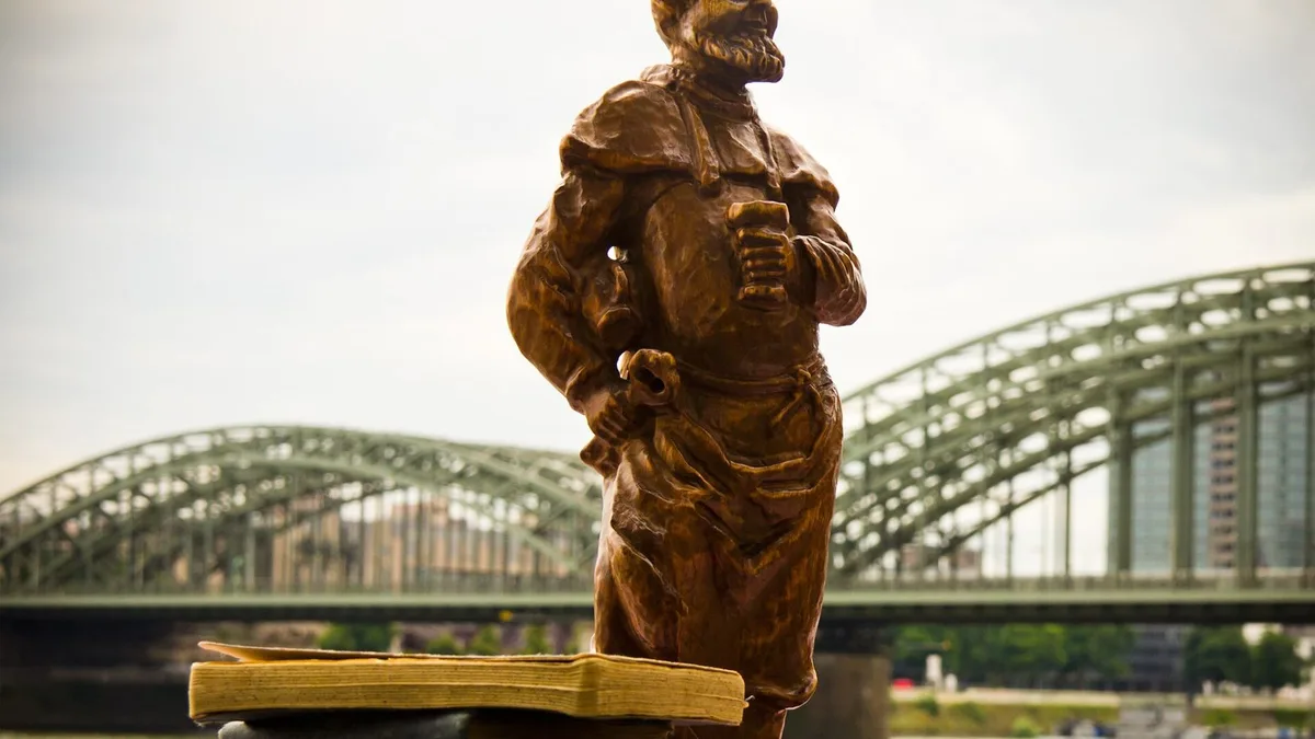 Holzfigur mit Kölschglas auf alten Büchern beim Altstadt-Flohmarkt, im Hintergrund die Hohenzollernbrücke